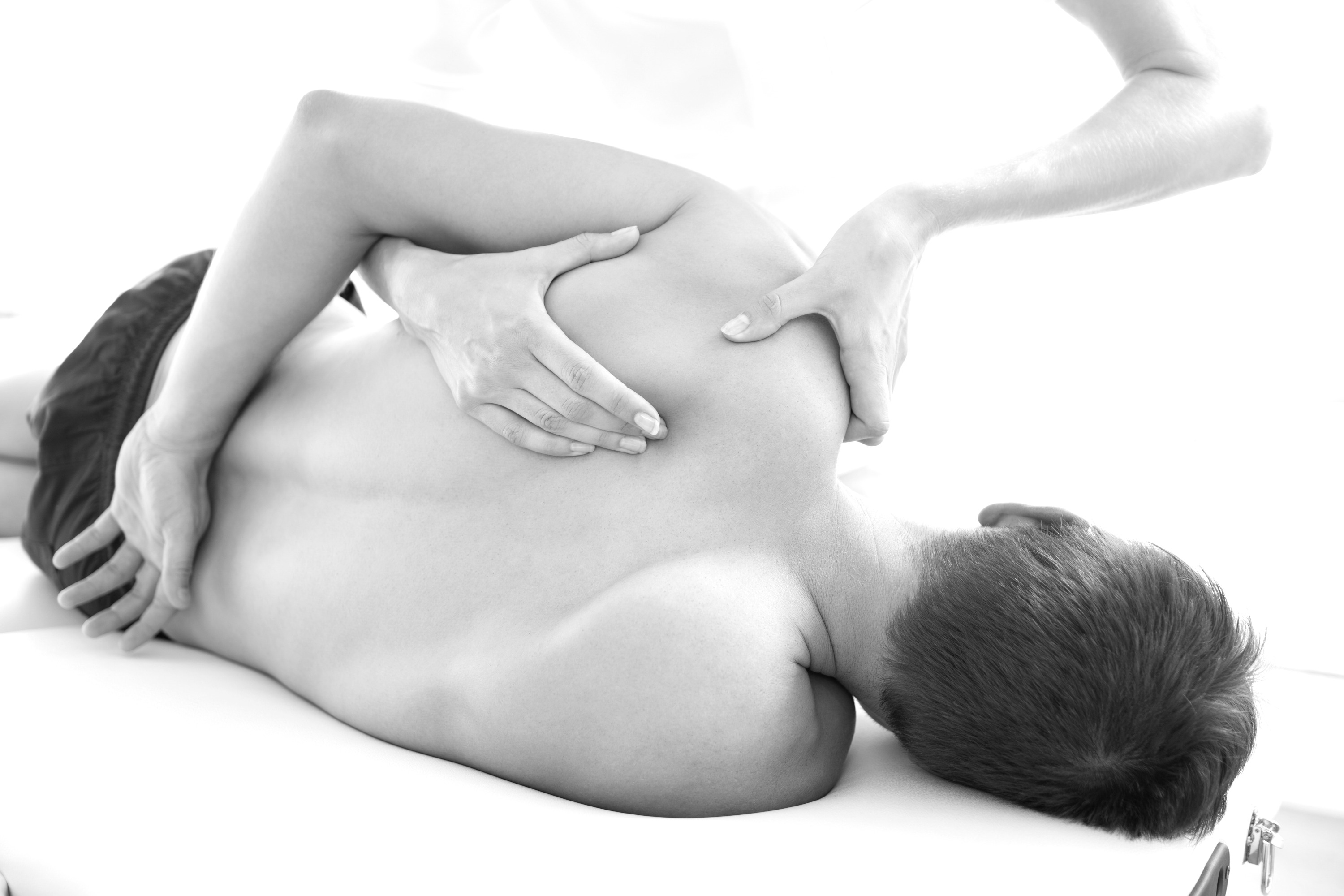 Hands applying focused massage to a client’s shoulder and upper back